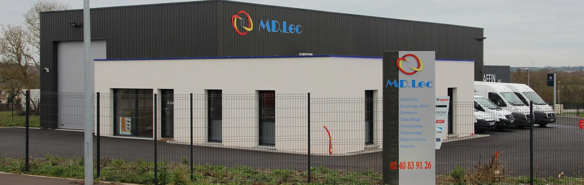 Bâtiment industriel MD.Lec avec véhicules garés.