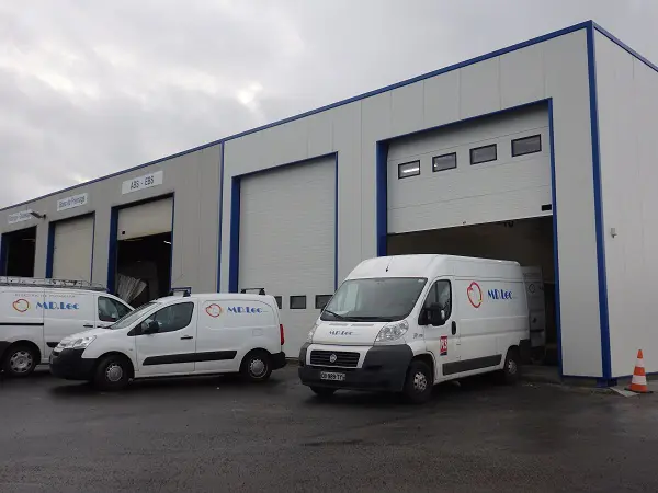 Bâtiment industriel avec plusieurs camionnettes garées devant.