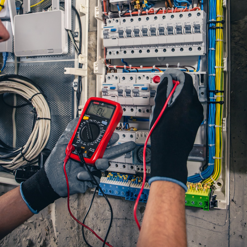 Électricien testant un tableau électrique avec un multimètre.