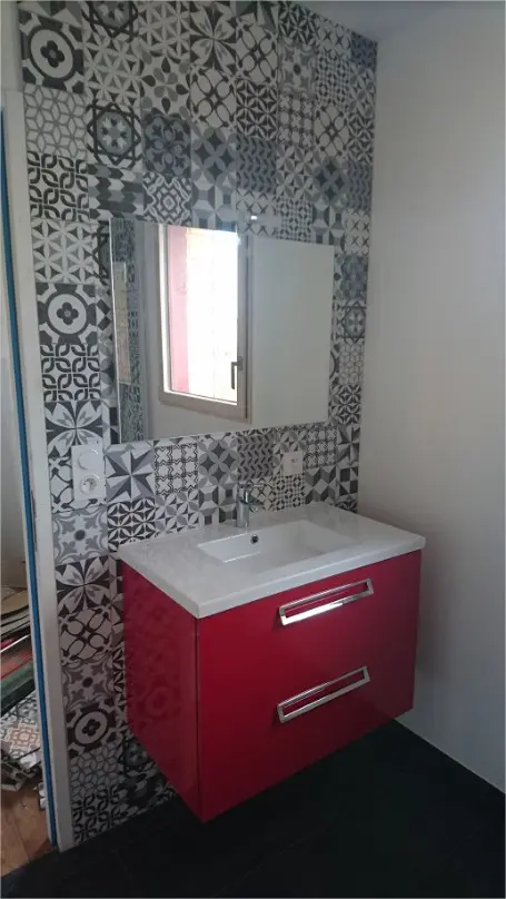 Salle de bain avec carreaux motif et meuble rouge.