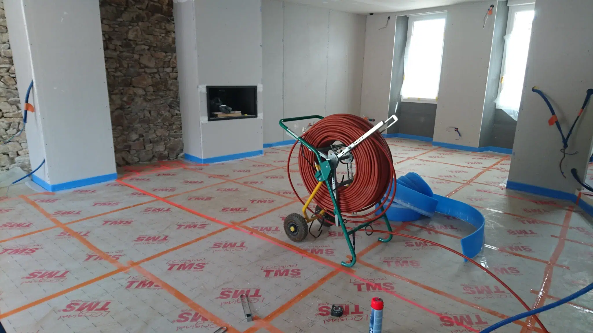 Salle en rénovation avec tuyaux et isolation au sol.