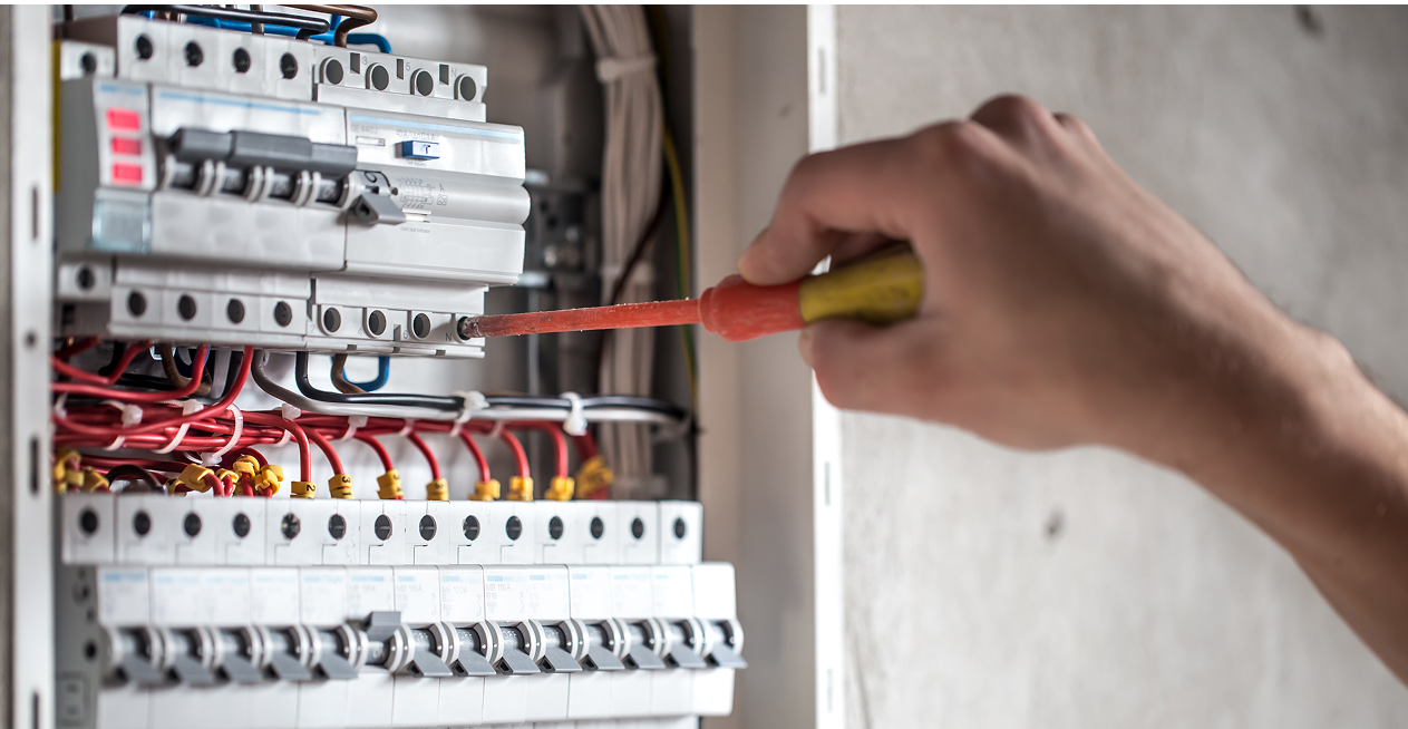 Main répare tableau électrique avec tournevis.